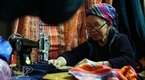 An old ethnic woman sews brocade products in the market.